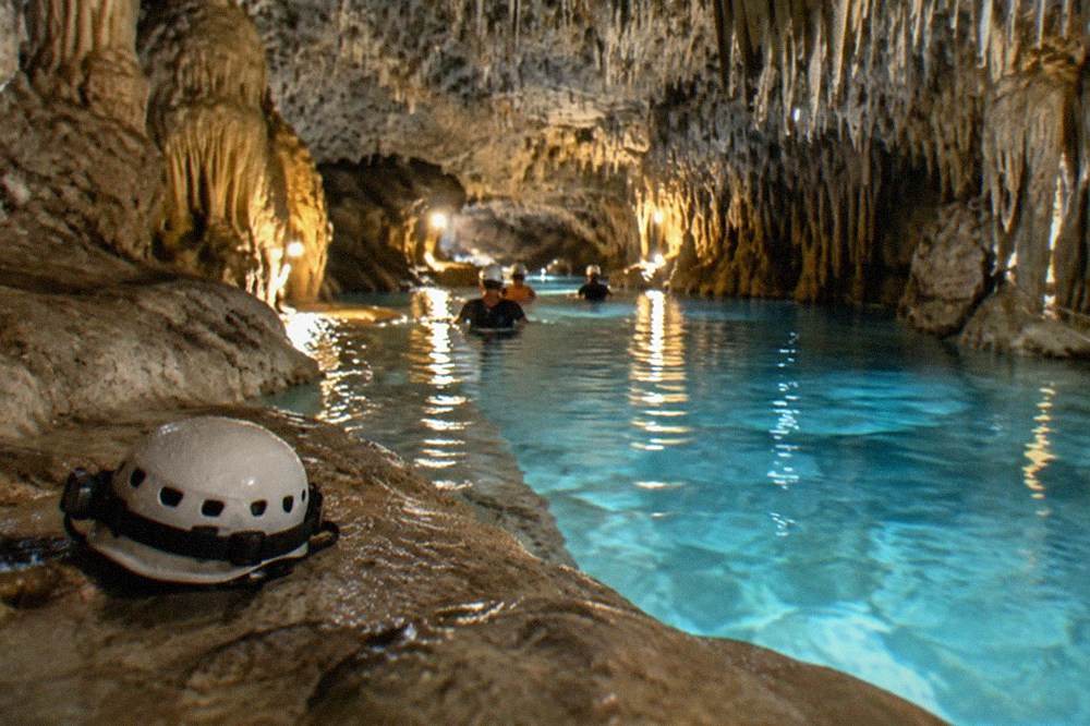 Clear blue cavern water lit by daylight through an opening in the rock ceiling