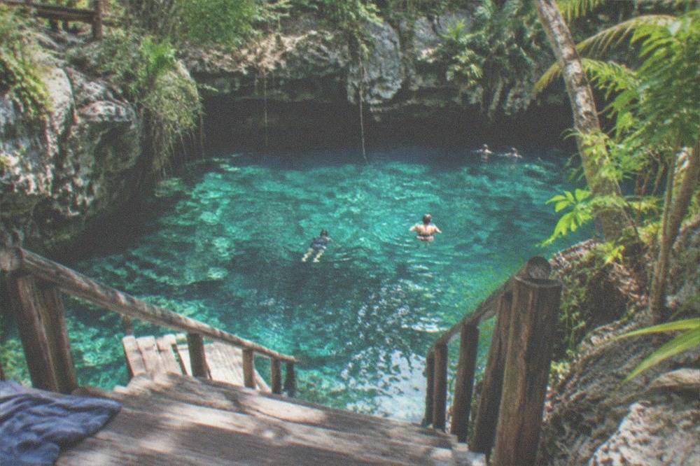 Wooden steps and platform leading down to clear turquoise cenote water between rocks