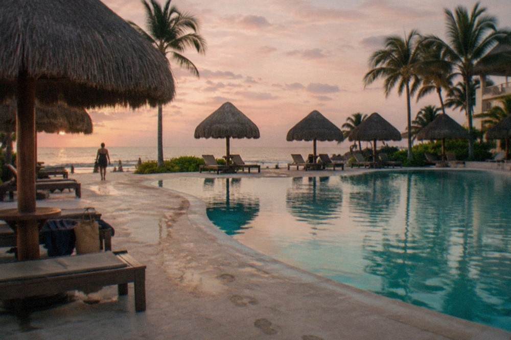 A resort pool deck with thatched umbrellas and calm water at sunrise