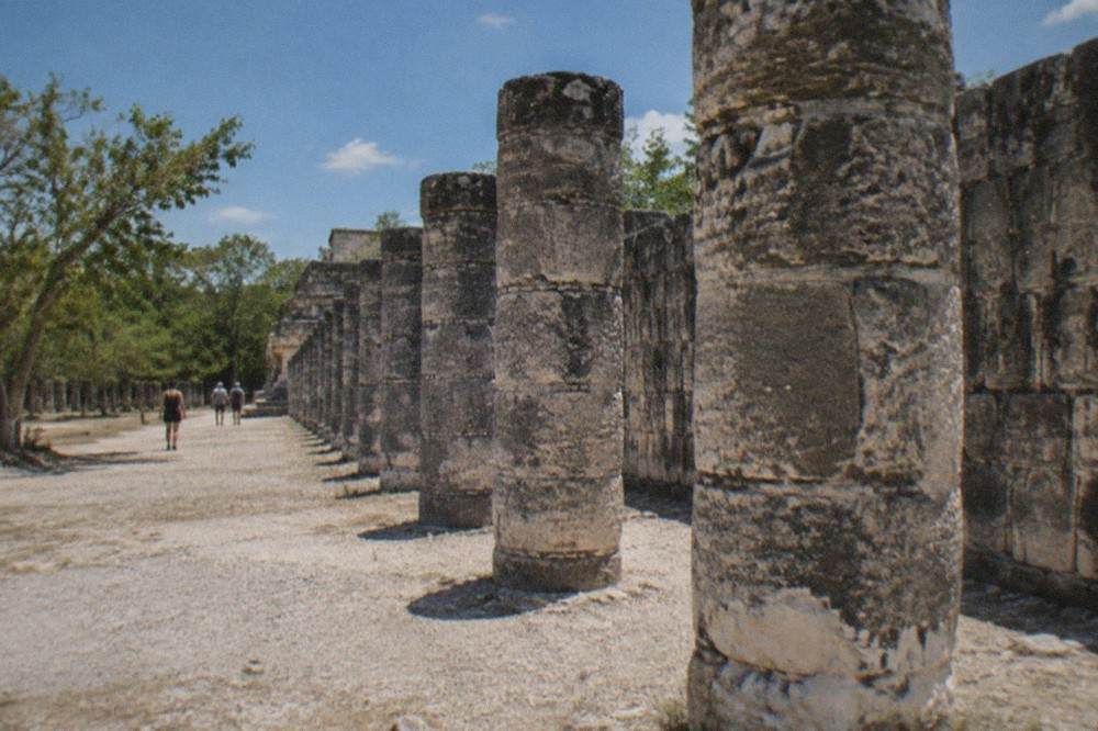 Stone columns of the Temple of the Warriors standing in a row beneath a clear blue sky