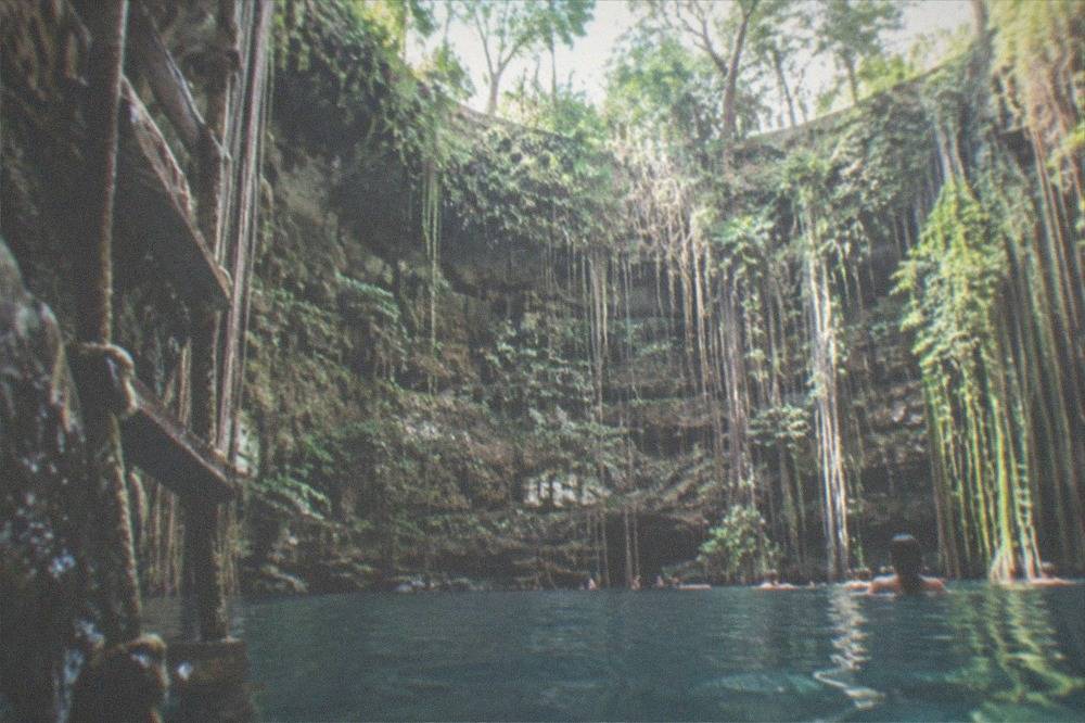The turquoise circular water of Cenote Ik Kil ringed by rock walls and hanging vines