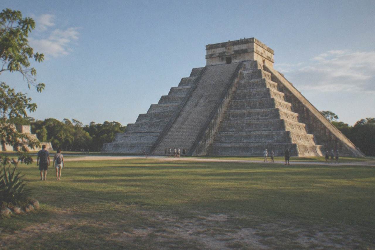 The stepped stone pyramid of El Castillo rising above a green lawn at Chichen Itza under a clear sky