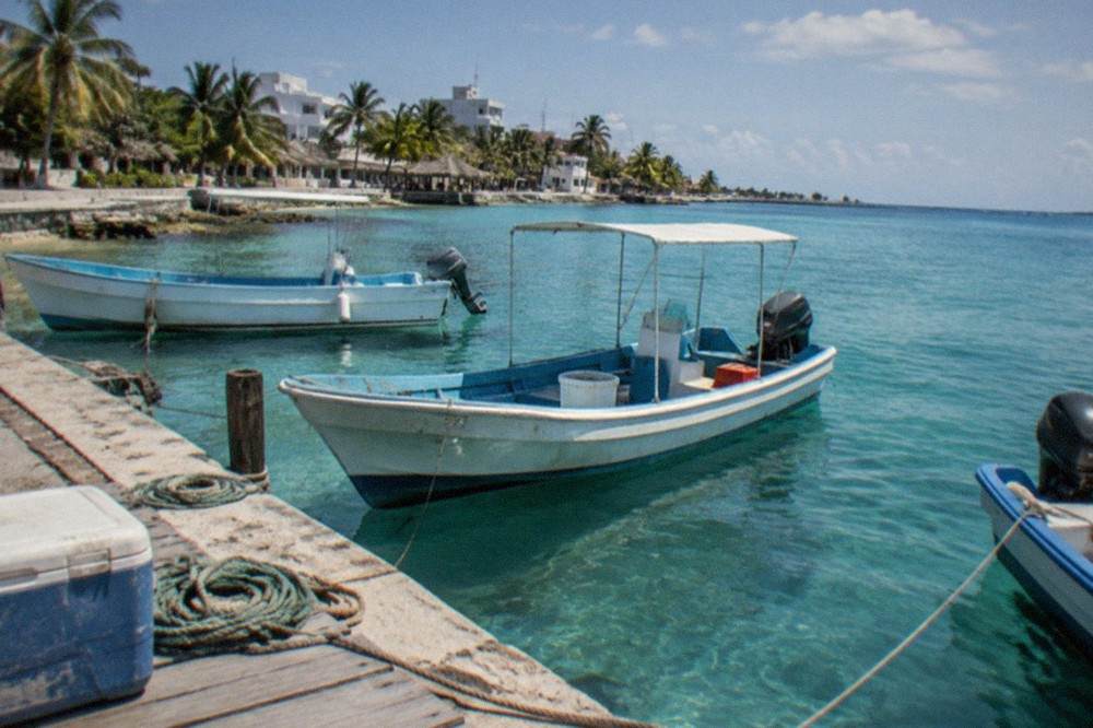 Fishing boats moored in calm water beside a Cozumel pier at midday