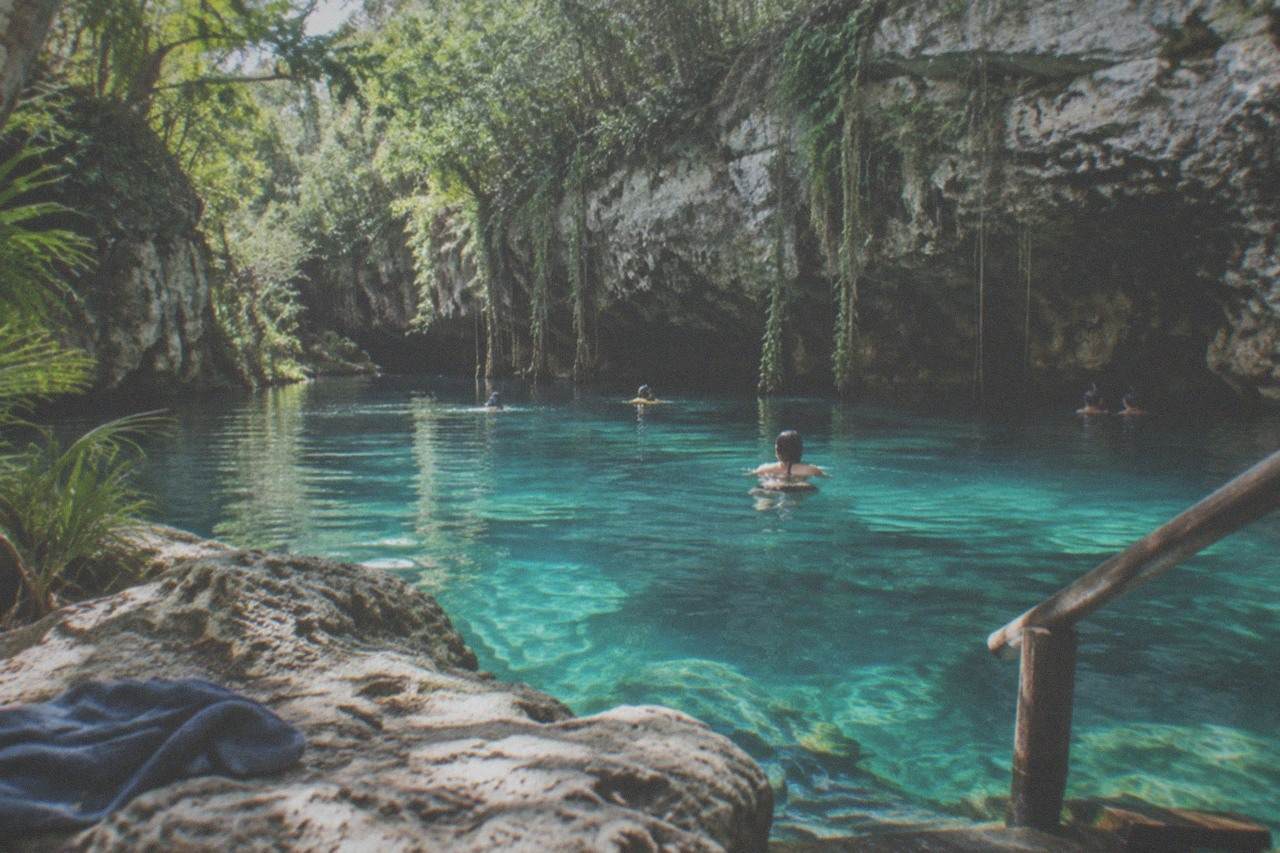 Clear turquoise water filling an open limestone cenote surrounded by jungle vegetation and exposed rock walls