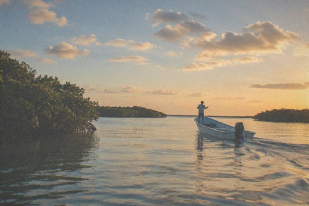 An open boat crossing a wide calm lagoon with mangrove islands and scattered clouds overhead