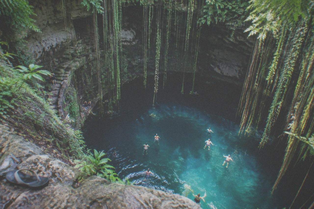 Clear turquoise water filling a open limestone sinkhole surrounded by jungle canopy and hanging vines