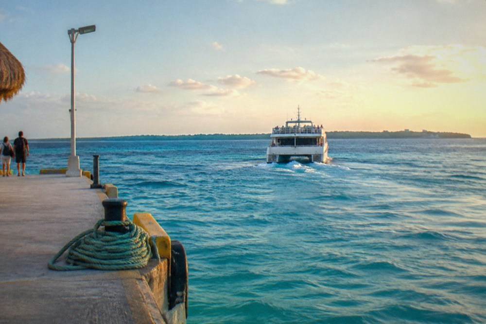 A passenger ferry crossing open turquoise water toward an island coastline
