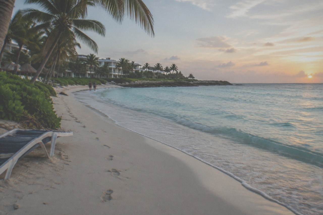 Quiet stretch of pale Caribbean sand with calm turquoise water and palm trees