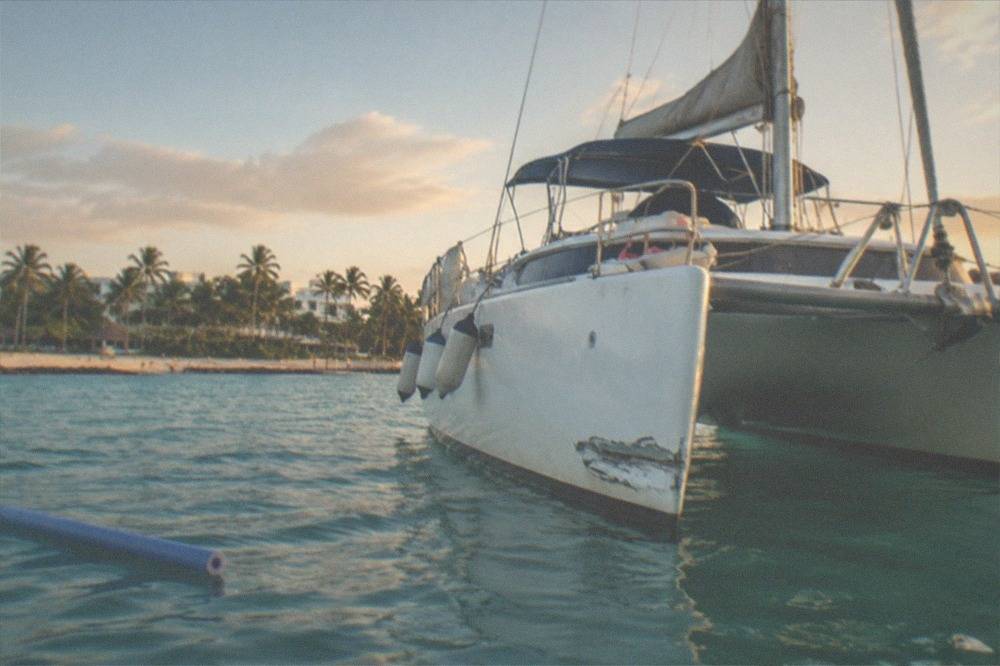 A white catamaran on calm turquoise water near a small island coastline