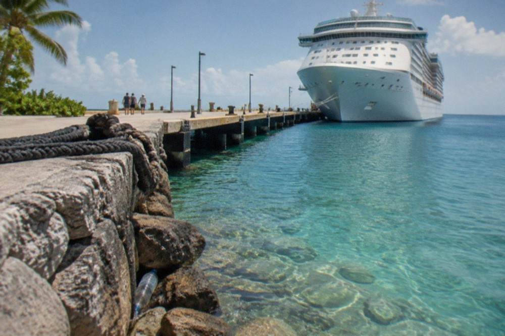 White cruise ship tied to a pier with clear shallow water and stone shoreline nearby