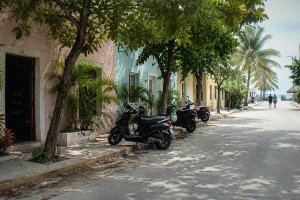 Quiet street in San Miguel de Cozumel with parked scooters and storefronts in the shade