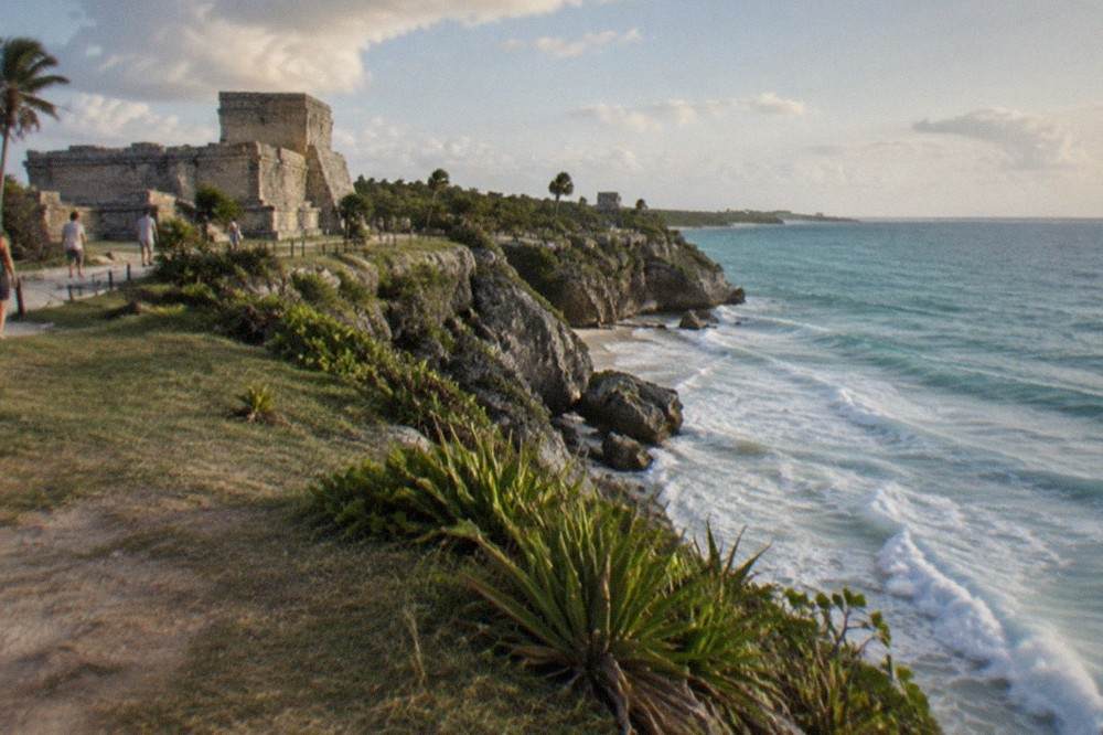 Wide view of the Tulum archaeological site with stone ruins on a grassy cliff above the Caribbean sea