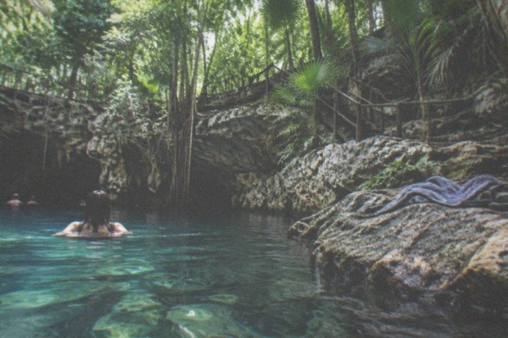 Clear open water in a jungle cenote surrounded by dense green canopy