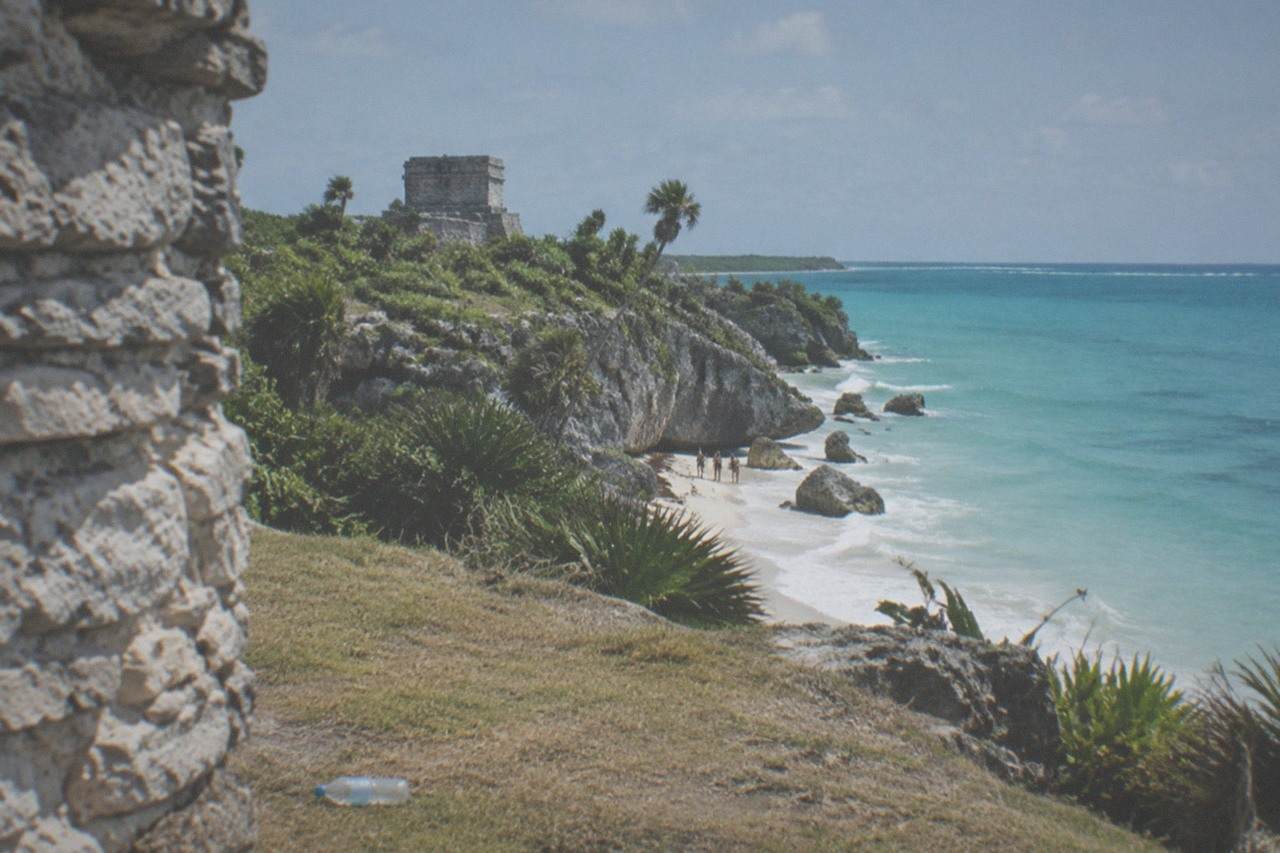 Mayan stone ruins on a grassy clifftop above turquoise Caribbean water