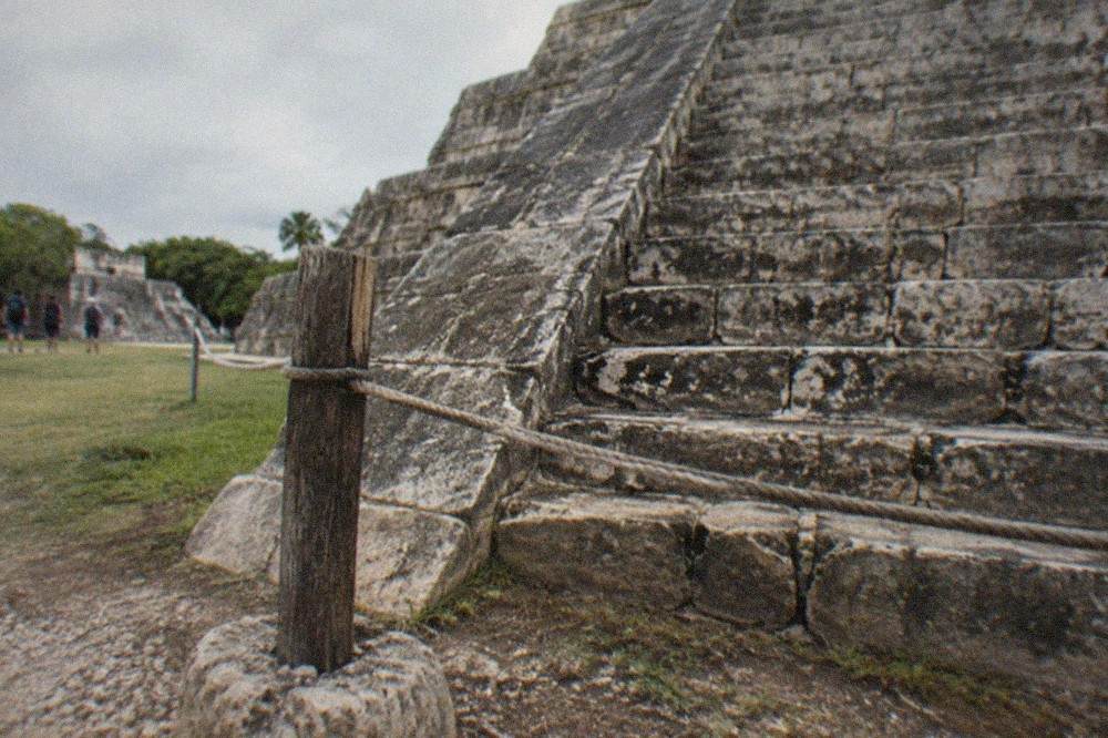 Roped-off staircase of a Maya temple pyramid with weathered stone steps and a wooden barrier in front