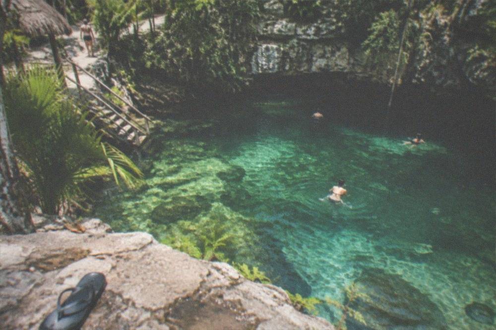 Clear freshwater cenote surrounded by limestone rock and jungle vegetation at midday