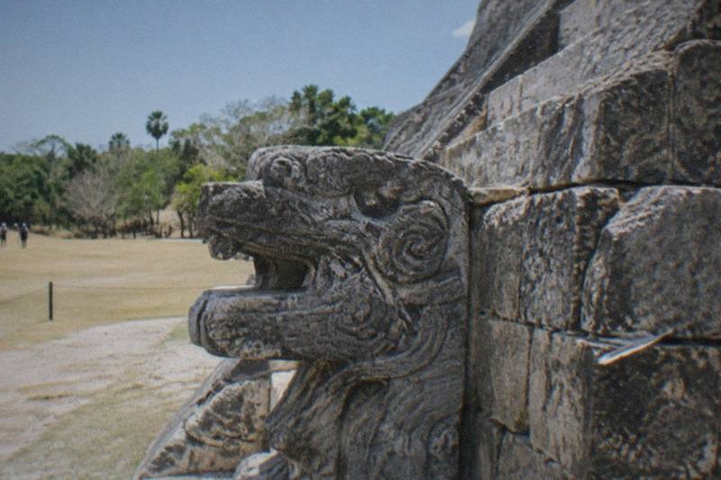 The stepped pyramid of Chichen Itza on an open plain under bright sky, carved stone facade in the foreground, no people.