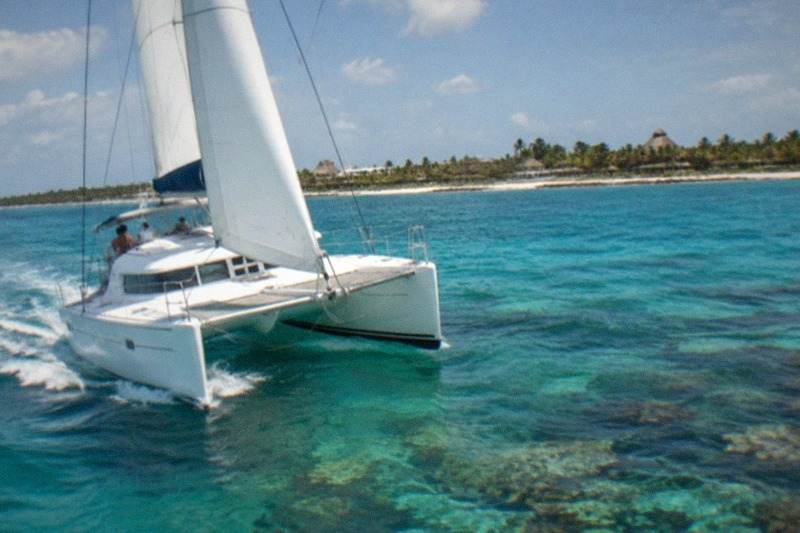 A Caribbean catamaran sailing on turquoise water off Cozumel, white sail and wake, coral-reef colors visible below the surface, no people.
