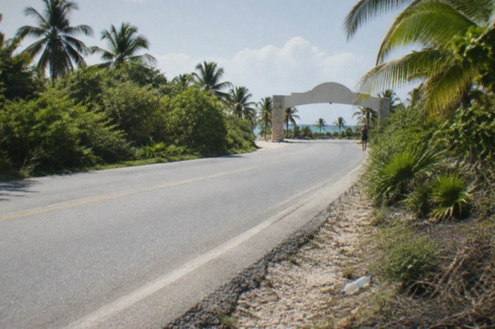 Coastal highway running south through palm trees toward a small beach town entrance arch