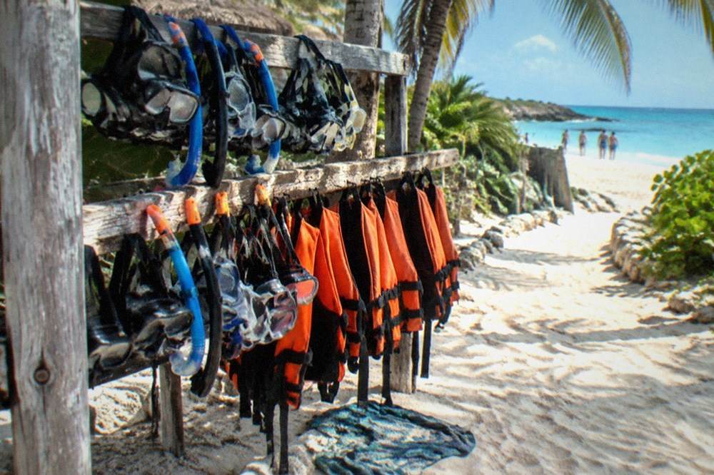 Snorkel gear and life vests laid out on a wooden rack beside a sandy beach path