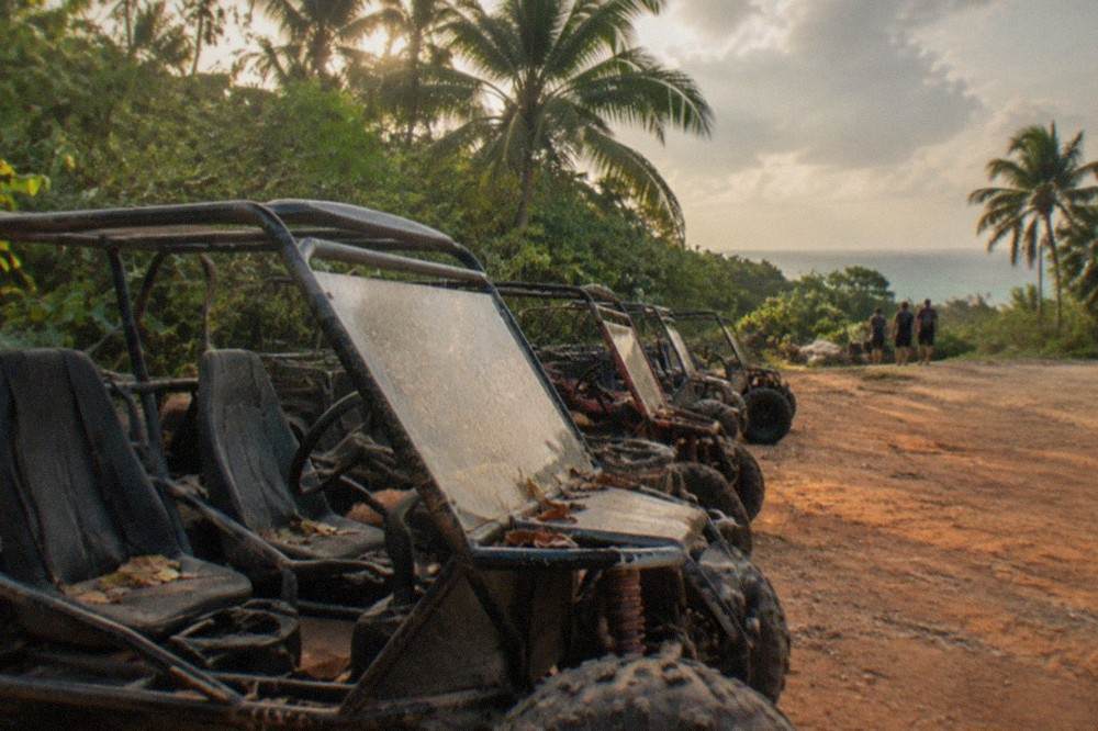 A line of open-frame dune buggies parked on a jungle dirt trail