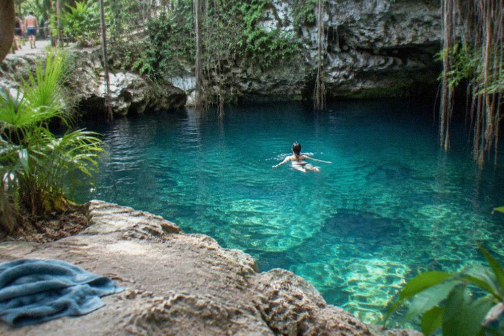 A swimmer floating in clear turquoise water inside an open jungle cenote