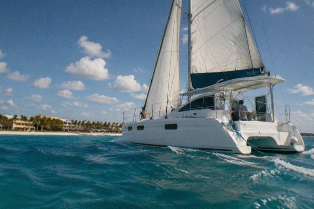 A catamaran under sail on open turquoise Caribbean water with scattered clouds