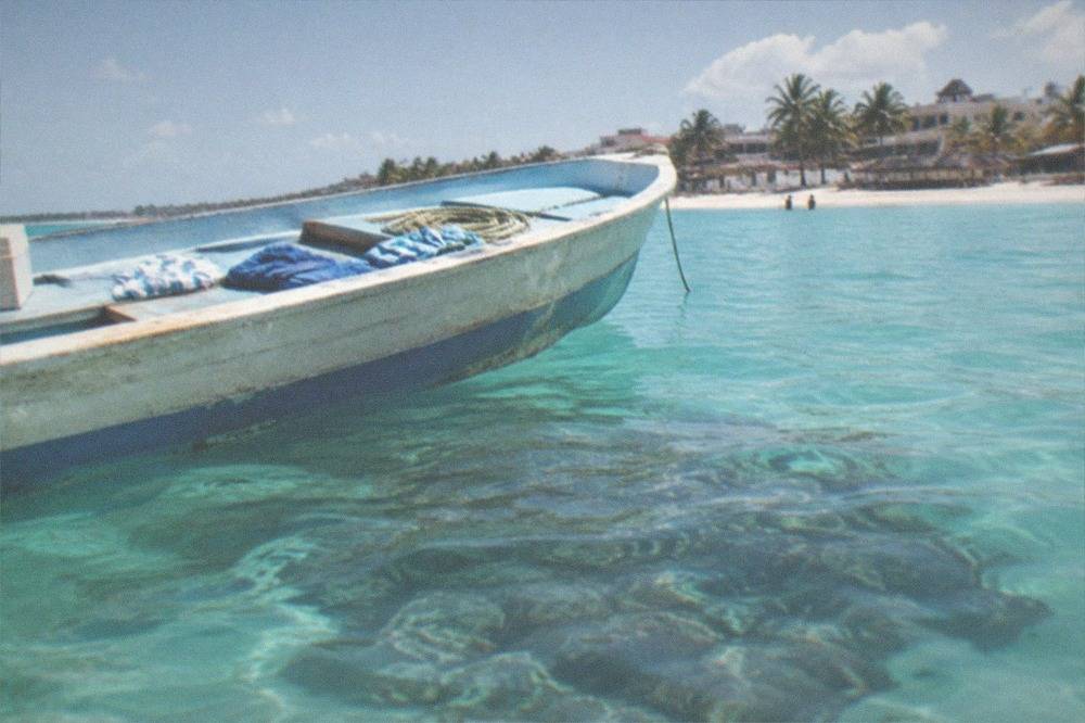 A wooden fishing boat on turquoise Caribbean water near a coral reef