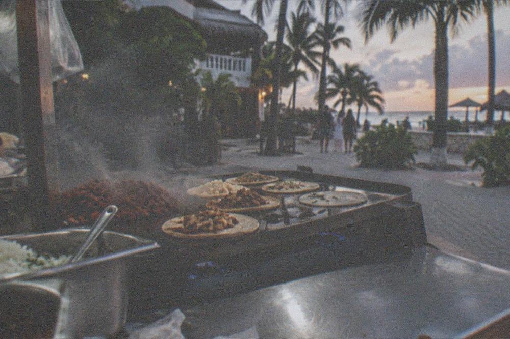 Steam rising from a street food grill with tacos cooking in the evening
