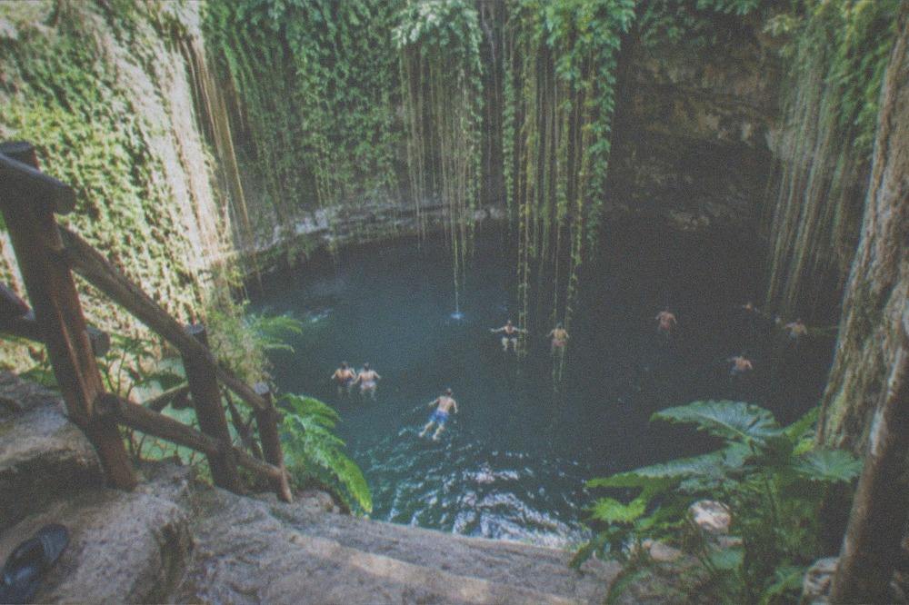 An open cenote pool surrounded by rock walls and jungle greenery