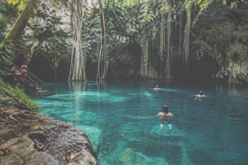 Clear turquoise water in an open cenote ringed by rock walls and hanging vines
