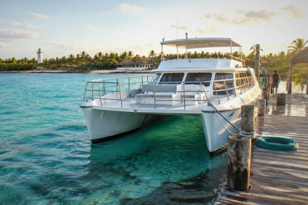 Passenger catamaran moored at a wooden dock with turquoise shallows and distant island palms.