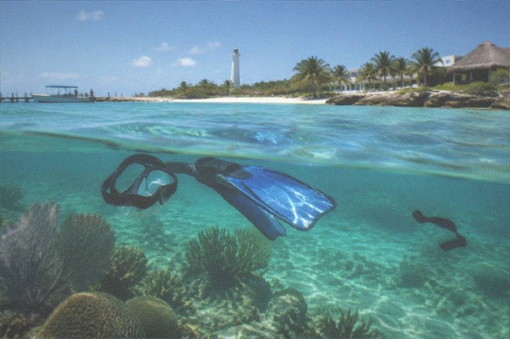 Snorkeler in calm turquoise water above a shallow reef with visible coral.
