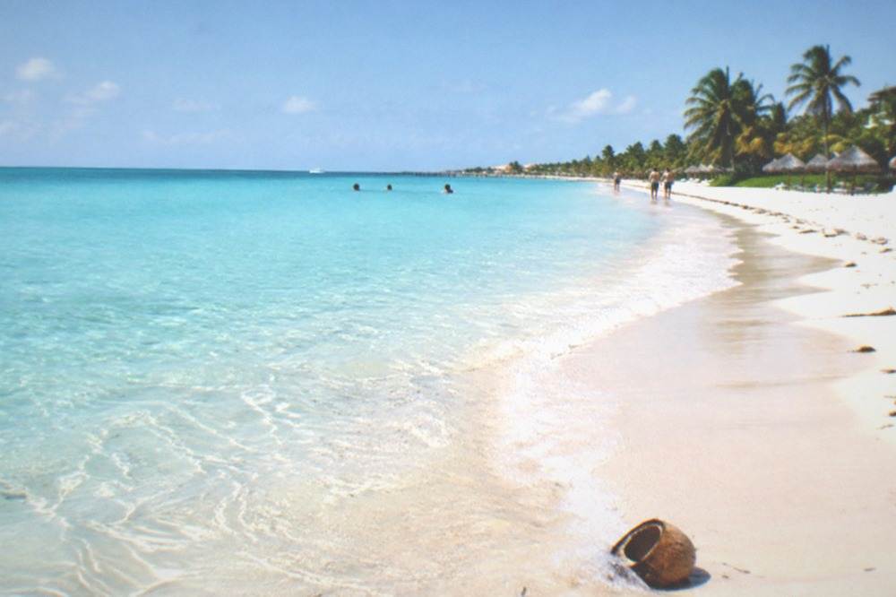 Wide shallow beach with pale sand and gently rippling turquoise water fading to the horizon.