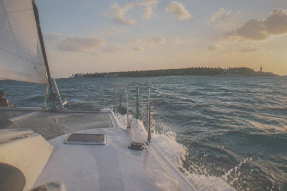 Catamaran under sail on open water with an island on the horizon