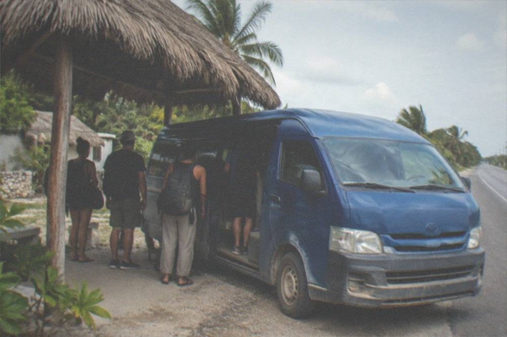 Blue passenger van parked at a roadside stand with passengers waiting to board