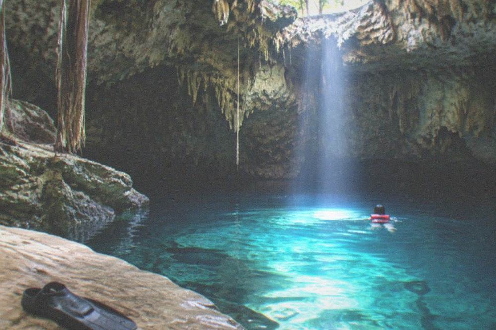 Underground cave pool lit by a shaft of daylight with a swimmer wearing a life vest