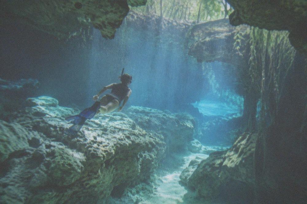 Snorkeler floating above a bright underwater cavern passage lit by sunlight