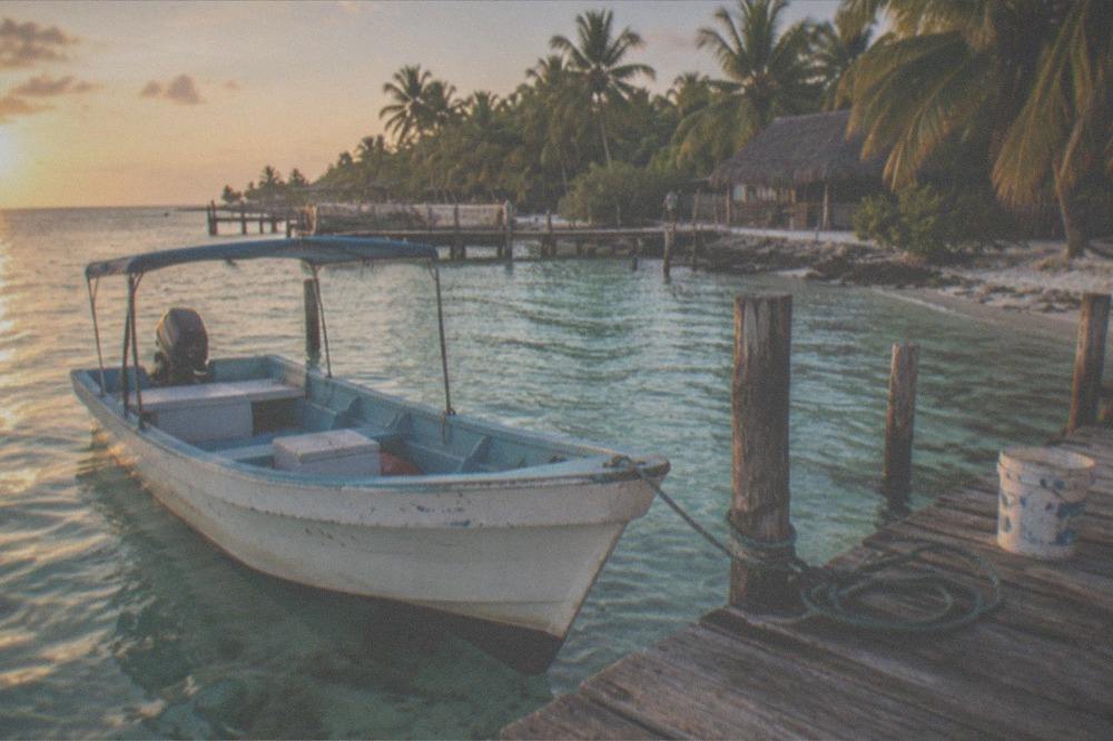 Wooden tour boat moored at a dock beside clear shallow water and palm trees