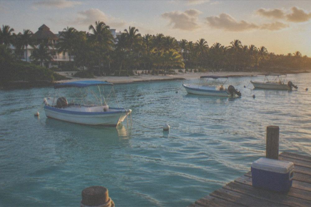 A calm turquoise bay with moored snorkel boats and a green palm-lined shoreline