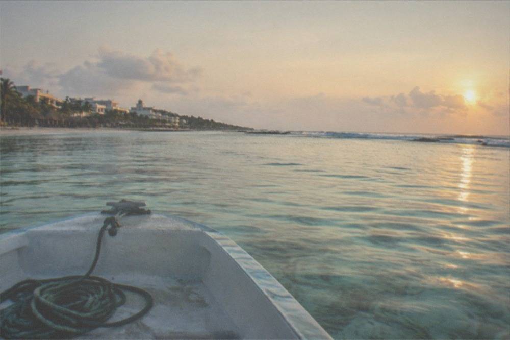A small boat crossing clear shallow water toward a reef line near the Riviera Maya coast