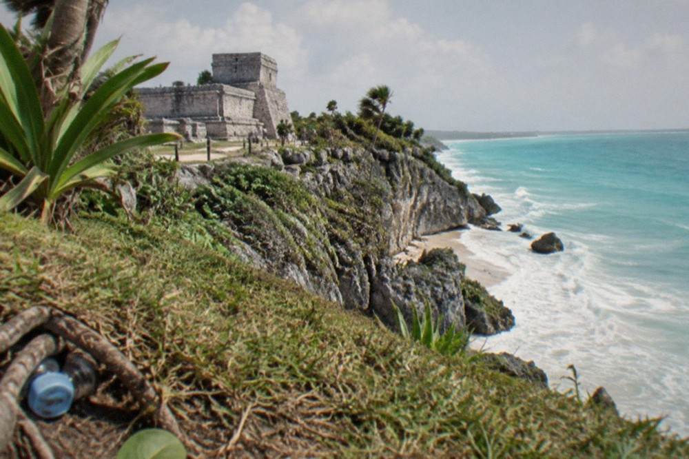 Turquoise Caribbean water below the pale stone walls of the Tulum ruins