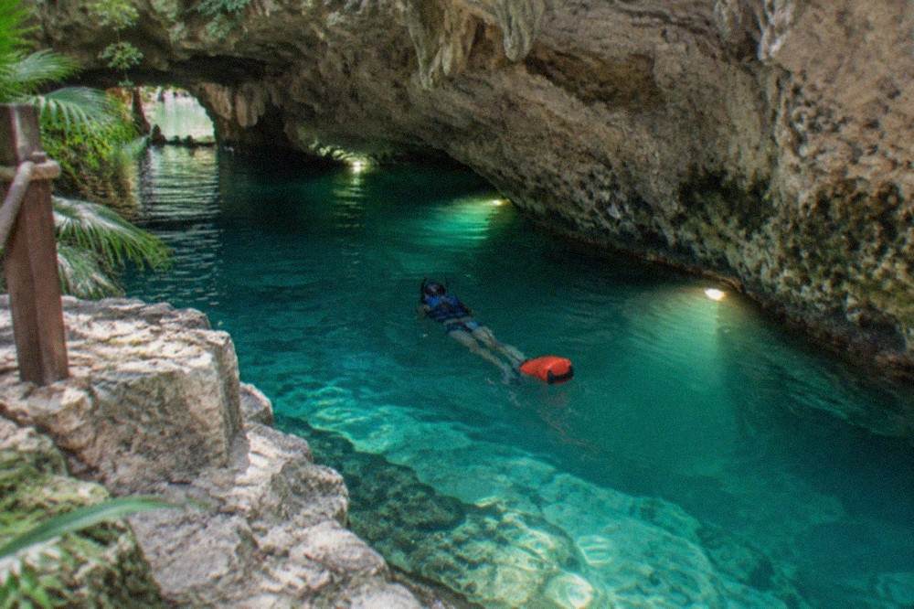 Swimmer with mask and life vest floating through a lit cavern section of an underground river