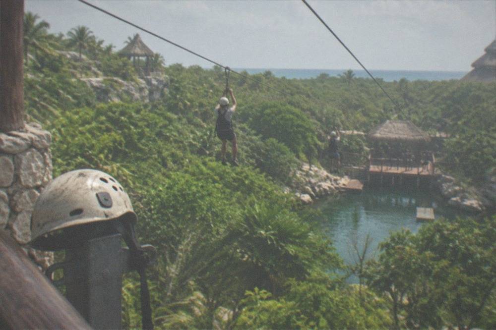 Zip-line riders crossing above jungle canopy toward a water landing platform